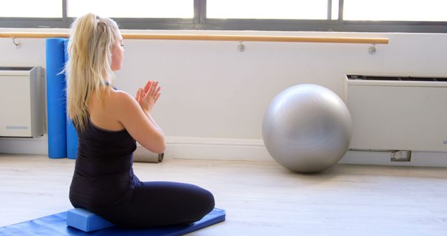 Woman practicing yoga meditation indoors sitting on a mat with hands in prayer pose. Useful for promoting fitness and wellness classes, yoga blogs, mental health articles, or relaxation products.