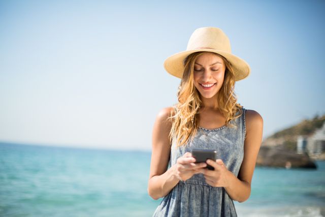Young woman smiling while using mobile phone at beach on sunny day