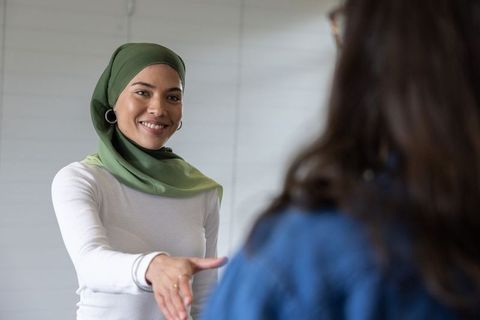 Smiling professional woman in green hijab extending handshake to coworker in office