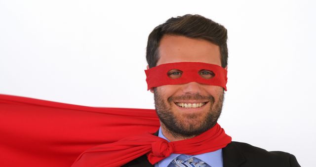 Businessman smiling with a confident look, wearing a red superhero mask and cape. Ideal for illustrating concepts such as leadership, success, confidence, and powerful business trends. Can be used in corporate presentations, motivational materials, and company websites.