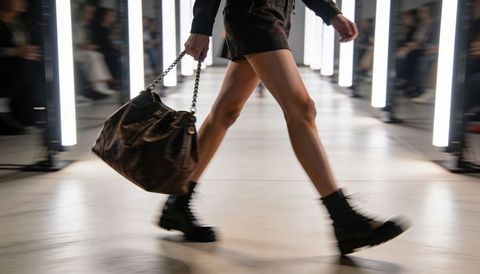 Striding runway model walking in combat boots carrying leather handbag with led pillars