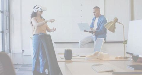 Woman Using White VR Headset in Bright Open Office While Coworker Works on Laptop