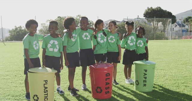 Portrait of happy diverse schoolchildren with recycling bins in sports field at elementary school. School, ecology and education, unaltered.