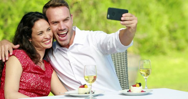 Couple enjoying a lunch date outdoors, taking a selfie together while smiling and laughing. Use for lifestyle, romance, outdoor living, and social media related projects.