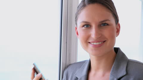 Business Professional Woman Smiling Near Window with Smartphone