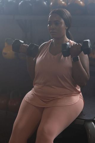 African american woman lifting dumbbells on bench in pink workout set, focused strength training