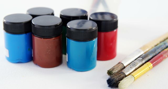 A collection of colorful paint pots alongside a set of used brushes, with copy space. Art supplies like these are essential for painters and hobbyists to create their artwork.