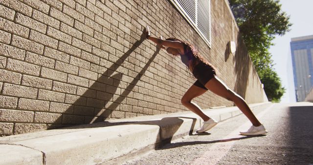 African american woman exercising outdoors leaning of wall and stretching in the city. healthy outdoor lifestyle fitness training.