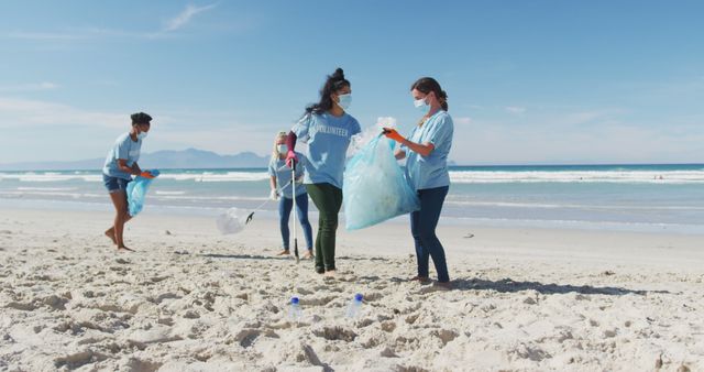 Group of volunteers wearing face masks, actively picking up trash on sandy beach, promoting environmental sustainability and teamwork. Ideal for use in campaigns about pollution prevention, community initiatives, environmental protection, and civic responsibility.