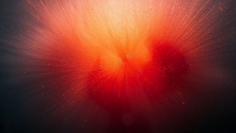 Radiating Core Emitting Orange-Red Light Rays and Glowing Particles in Abstract Gradient