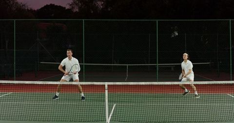 Dusk doubles tennis players in white uniforms on outdoor hard court showcasing teamwork
