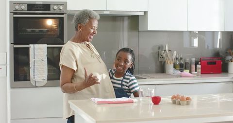 African grandmother and granddaughter laughing while baking together in bright kitchen