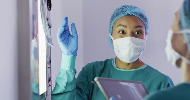 Image of biracial female surgeon discussing x-ray with colleague in operating theatre. Hospital, medical and healthcare services.