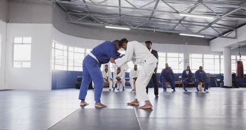 Martial artists grappling in dojo under referee