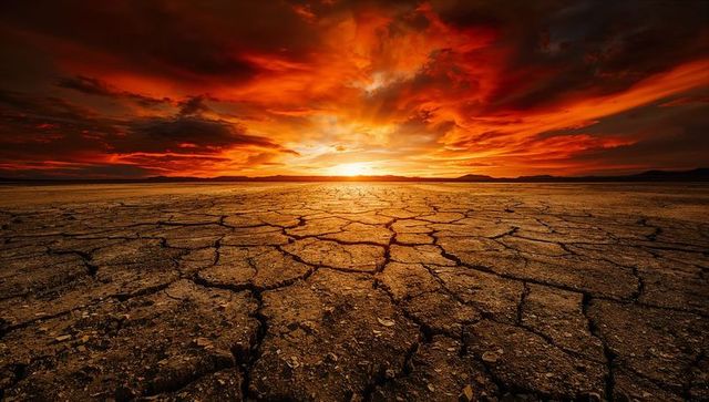 Cracked desert floor radiant sunset with fiery red sky and sunburst on horizon
