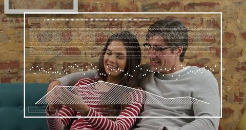 Couple relaxing on teal sofa holding tablet with data overlay and exposed brick backing