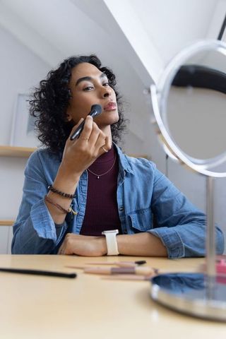 Non-binary person applying makeup at vanity mirror for everyday self-care routine