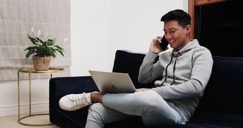 Young Man Engaging in Remote Work at Home Using Smartphone and Laptop