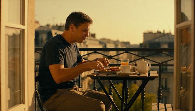 Man enjoying quiet balcony breakfast with teapot, orange juice and urban rooftop view