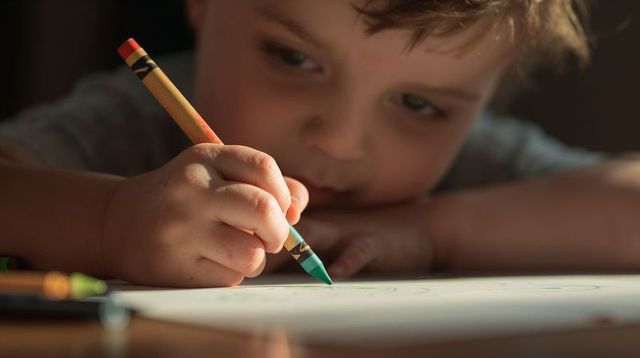 Young boy drawing with green crayon close-up showing creative focus and fine motor skill