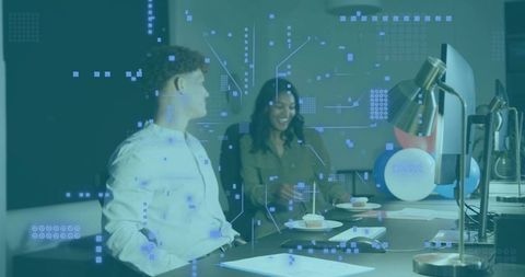 Collaborating young professionals sharing ideas at tech desk with HUD overlay and cupcakes