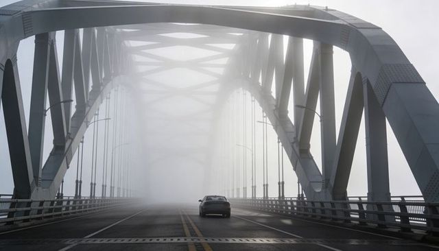 Solitary sedan crossing steel-arch bridge in dense fog moody urban transport journey