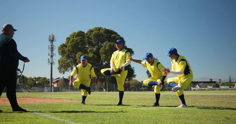 Adult baseball team stretching in bright yellow uniforms during outdoor warmup with coach