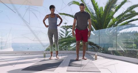 Workout partners stretching on sunlit coastal terrace with yoga mats and ocean view