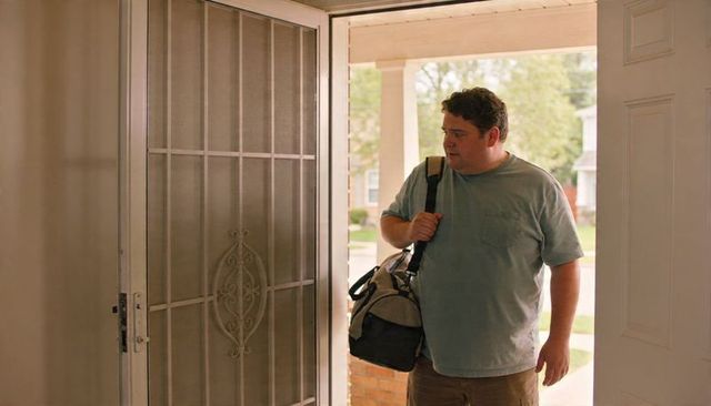 Man pausing at front door carrying duffel bag at suburban home entrance with copy space