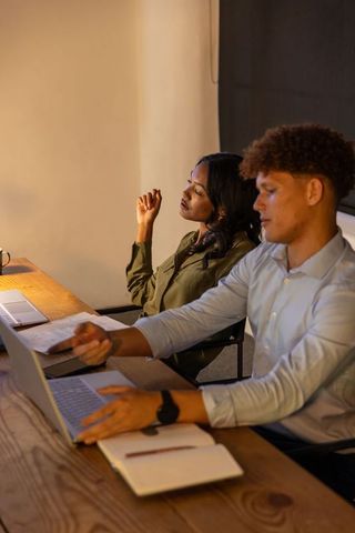 Diverse coworkers collaborating late at office desk with laptops, documents and coffee