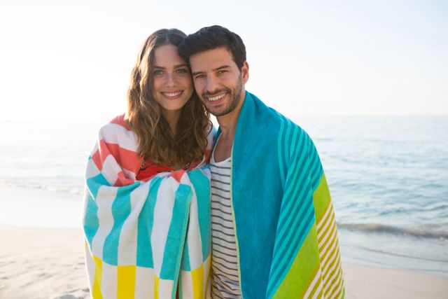 Portrait of happy young couple wrapped in blanket at beach - Download Free Stock Photos Pikwizard.com