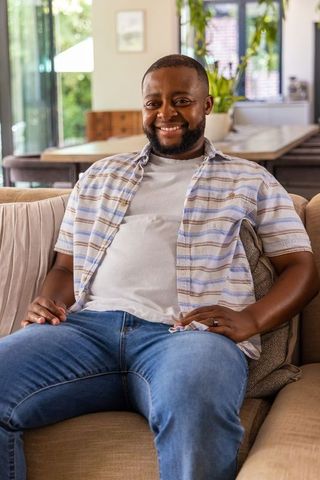 Relaxed african american man smiling on beige sofa in sunlit modern living room