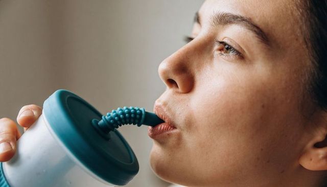 Calm woman sipping from reusable cup with teal lid and textured silicone straw, closeup