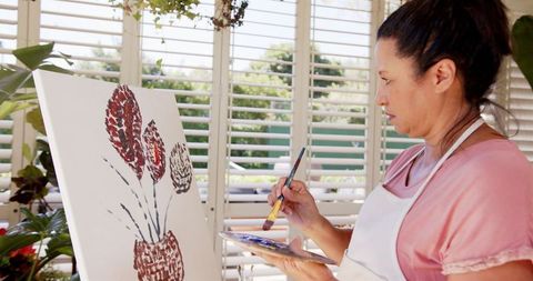 Woman artist painting floral artwork in sunlit studio