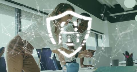 Businesswomen Collaborating on Cybersecurity Strategy with Holographic Shield Overlay