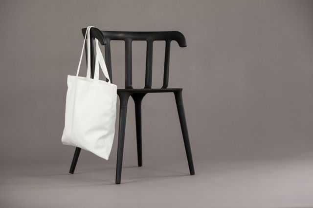 White shopping bag hanging on black chair against grey background