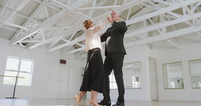 Senior couple elegantly ballroom dancing in bright studio with white walls and natural light. Ideal for use in articles or ads focused on active lifestyles for seniors, ballroom dancing classes, or aging gracefully.