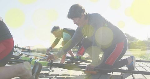 Mature female rower kneeling adjusting neon green oarlock on dock in bright sunlight in red leggings