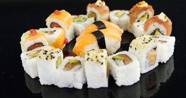 An assortment of sushi rolls is presented on a reflective black surface, showcasing a variety of fillings and toppings. Sushi, a traditional Japanese dish, is enjoyed worldwide for its fresh flavors and artistic presentation.