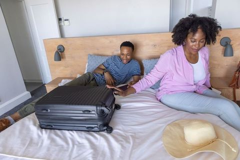 African american couple packing for weekend getaway on bed reaching toward black suitcase