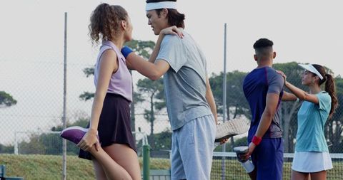 Young tennis players stretching in pairs on outdoor court wearing visors with water bottles