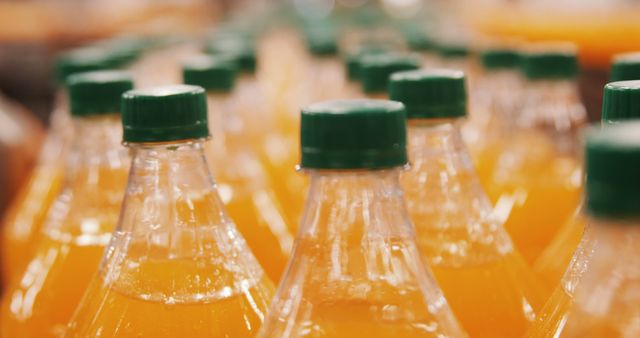 Rows of orange juice bottles with green caps, viewed from a close-up angle. Ideal for use in advertisements, grocery store promotions, food and beverage industry promotions, and highlighting freshness and health benefits of consuming fruit juices.