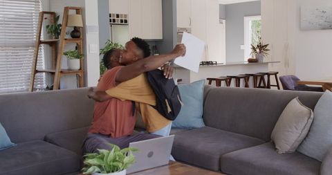 African american father and teen son hugging on grey sofa celebrating homecoming reunion