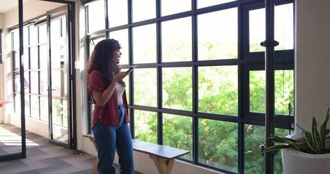 Young african american woman speaking into smartphone at office grid window with greenery