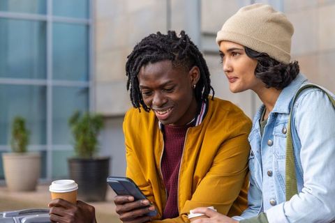 Young diverse friends sharing coffee and smartphone outside modern office building