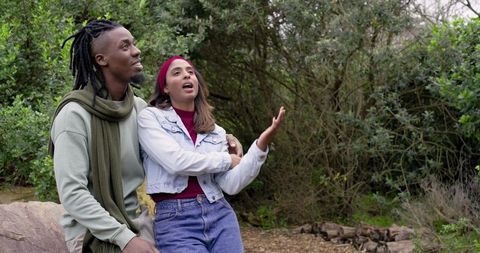 Diverse Couple Singing and Laughing While Sitting on Rock in Woodland Embracing Moment