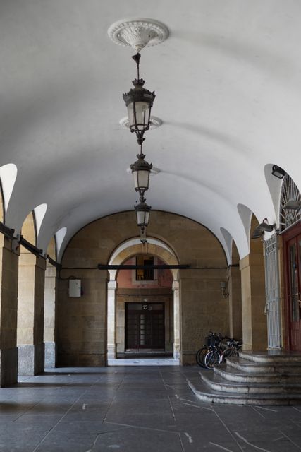 Arched corridor with historical lanterns, stone pillars, and a serene atmosphere. Suited for themes on architecture, Mediterranean charm, urban exploration, historical preservation, tourism, and tranquility.