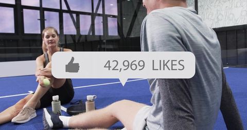 Two athletes resting on indoor blue court holding tennis ball with social likes overlay