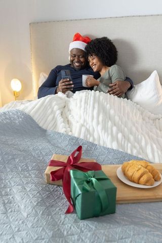 African american couple celebrating cozy christmas morning wearing santa hat holding mug and gifts