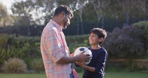 Father Teaching Son Soccer Skills on Sunlit Backyard Lawn